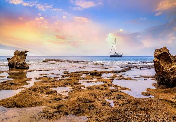 Beach sunset at Neil island Andaman India with naturals rocks and corals and sailing vessel at the horizon