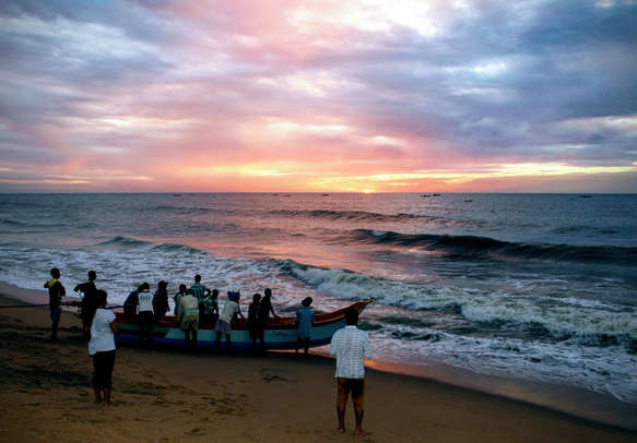 Fishermen going on a boat in the ocean for fishing during morning sunrise at Auroville Beach