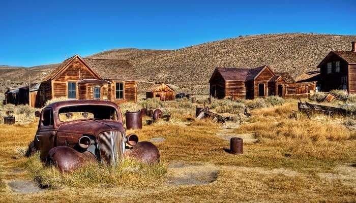 A photo capturing an old car and ruins of the houses in the abandoned town of Bodie in California