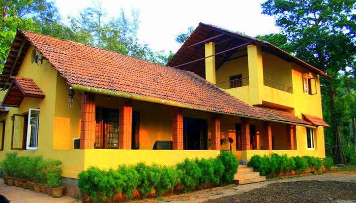 a Karnataka style home painted yellow and red with plants on the verandah