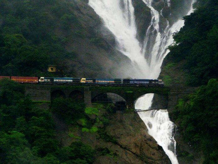 A train passes by on the railway track with the majestic Dudhsagar falls in the background