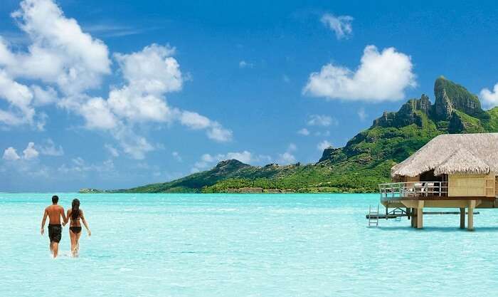 A couple walks on the not-so-deep ocean bed near their overwater villa