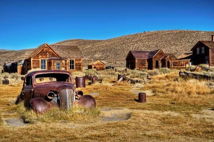 A photo capturing an old car and ruins of the houses in the abandoned town of Bodie in California