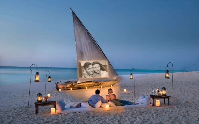 a couple sitting on white sand beach watching an old movie