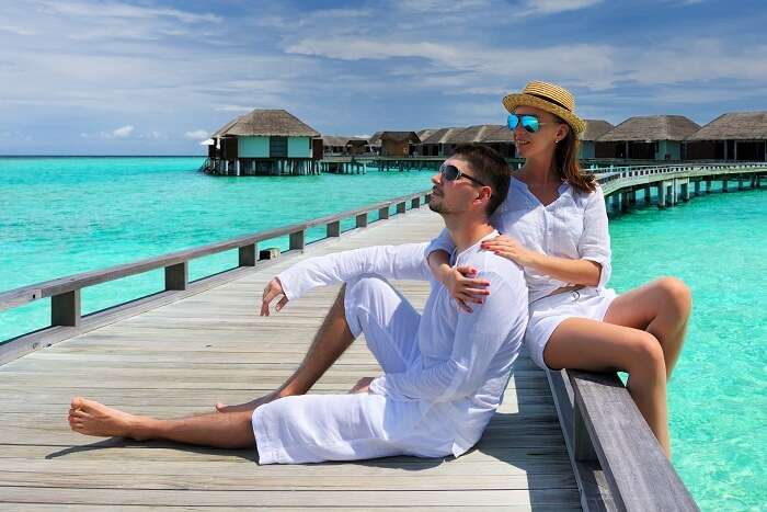 A couple on a jetty in front of the overwater properties on an island resort in Maldives