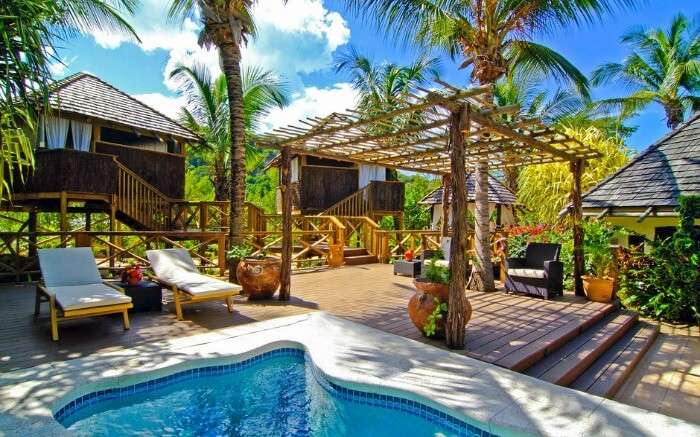 a small outdoor pool with two cabanas under the shade of palm trees 