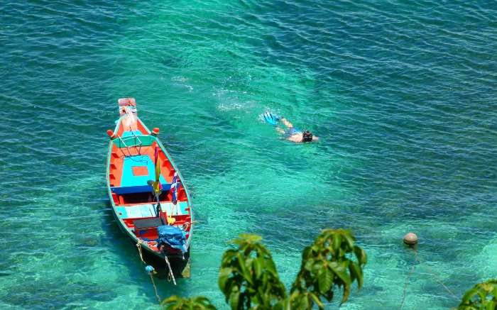 A guy swimming beside a colourful boat in blue waters