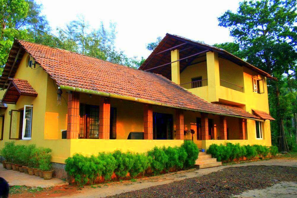 a Karnataka style home painted yellow and red with plants on the verandah