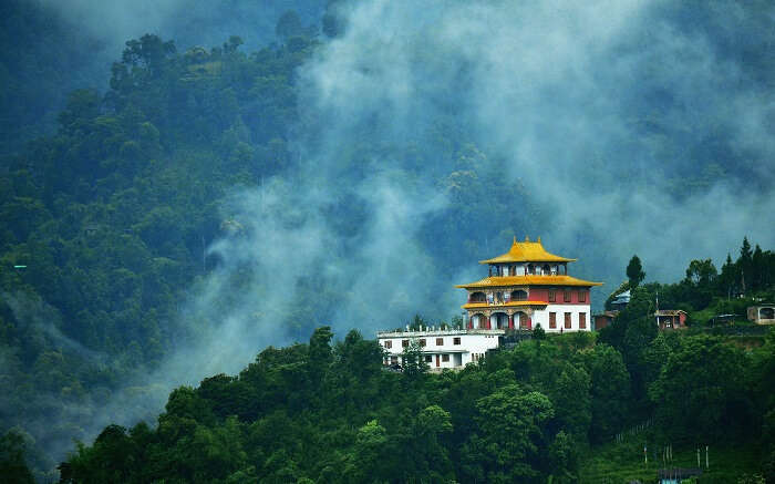 View of a monastery in Sikkim surrounded by lush greenery and fog