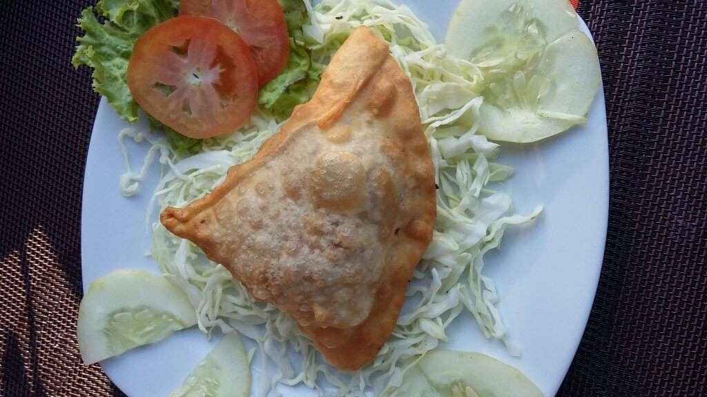 a samosa served with cabbage and tomato