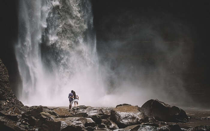 a couple standing below a waterfall
