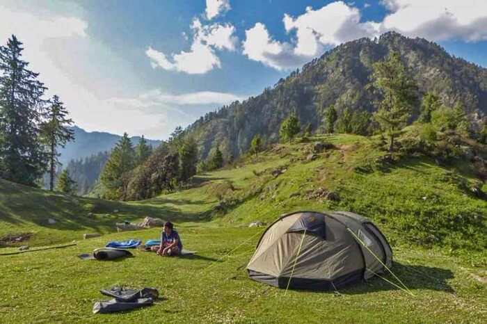 a girl sitting in a meadow beside a tent