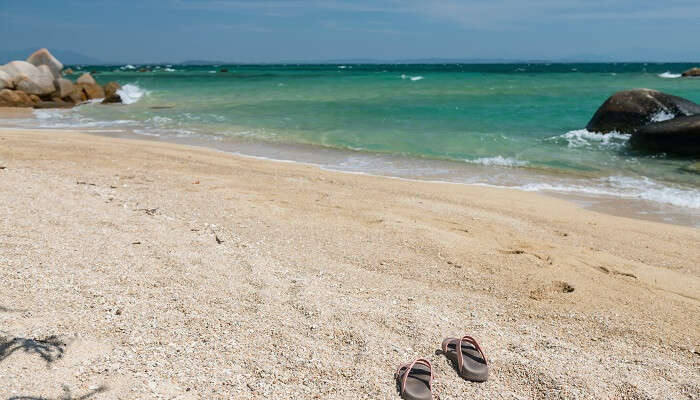 Flip flops on sand beach with stone arch