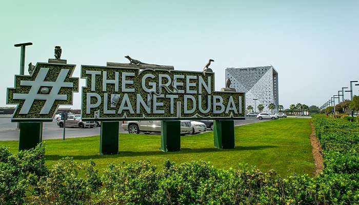 The Green Planet sign at City Walk with a blue sky and greenery around the foreground.
