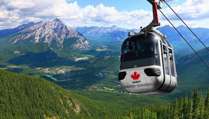 Sulphur Mountain Gondola on a blue sky with snow-peaked Rocky Mountains in Banff, among the smallest towns in Alberta