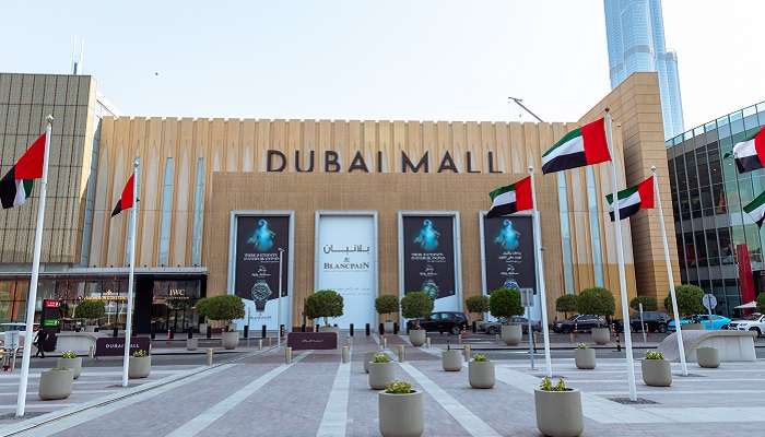 A view of the Dubai Mall, one of the top places to visit in Dubai during summer, with waving flags of the U.A.E.