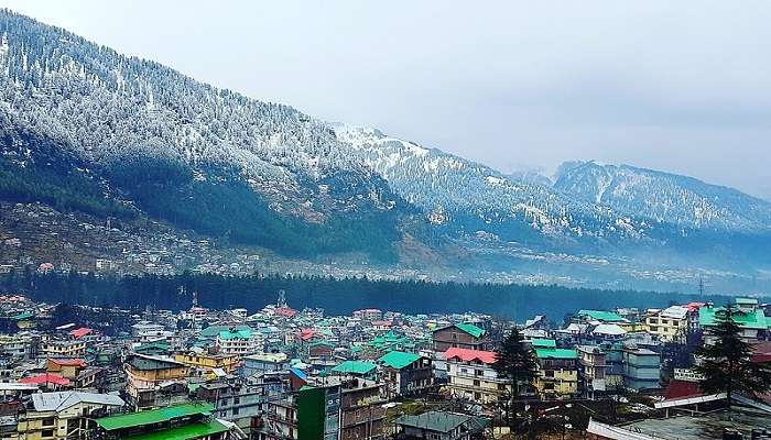 The trip to Manali has snow-covered mountains on one side and dwellings on the other.