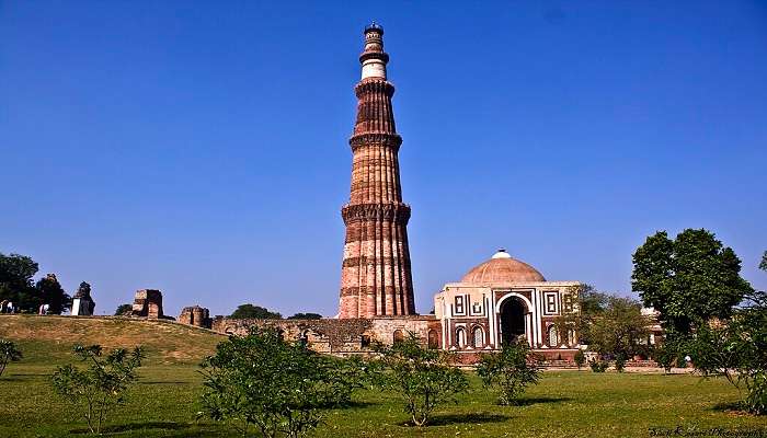 The quiet and peaceful atmosphere of Qutub Minar, a historical place to visit near Red Fort, is enveloped in green foliage.