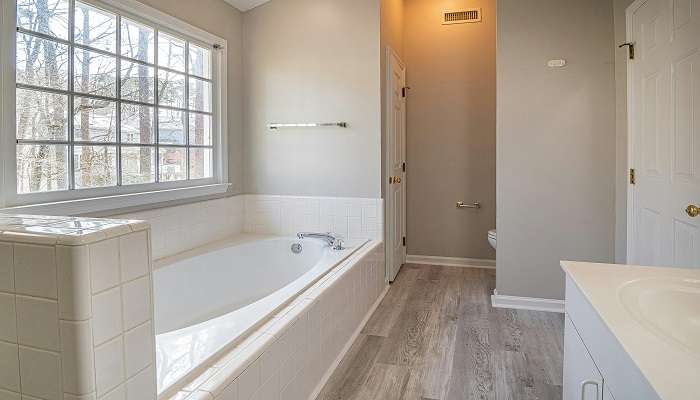 A white bathtub in the cottage bathroom with a full wall window of nature