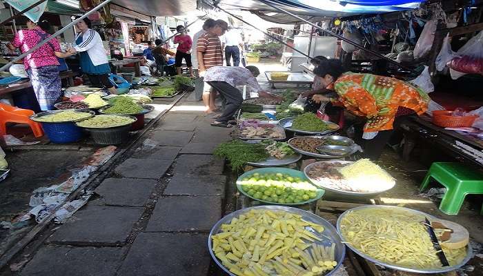 Visitors to Thailand enjoy the crowded Maeklong Railway Market where people shop by walking on the railway tracks with vendors selling food items and other products along the tracks.