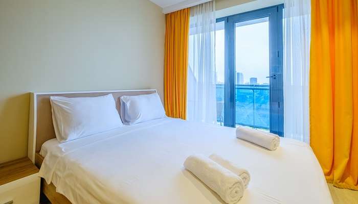 A comfortable bed with orange and white curtains at the blue window in the hotels in Nellore.