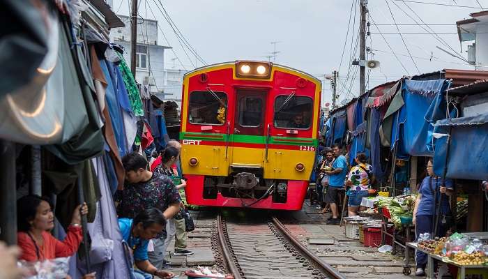 People rush around taking pictures and shopping for fresh food in the famous Maeklong Railway Market in Thailand near Bangkok when a train comes through the market, making it a popular tourist attraction.