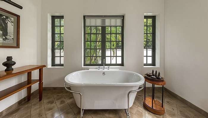 The white colored bathtub in the open area surrounded by trees and mountains