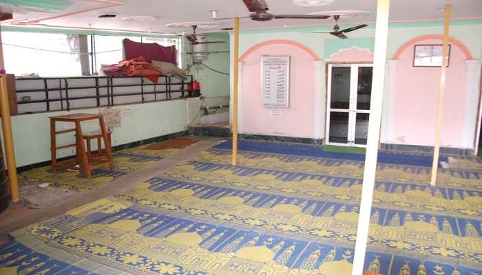 A well-maintained room in Hanuman Dharamshala with a red bed and white walls along with a window in the room