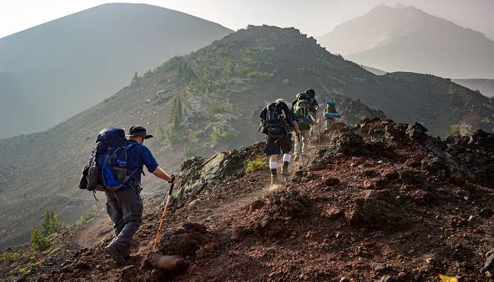 Two mountaineers equipped with backpacks, trekking poles, and warm clothing walk up the mountain.