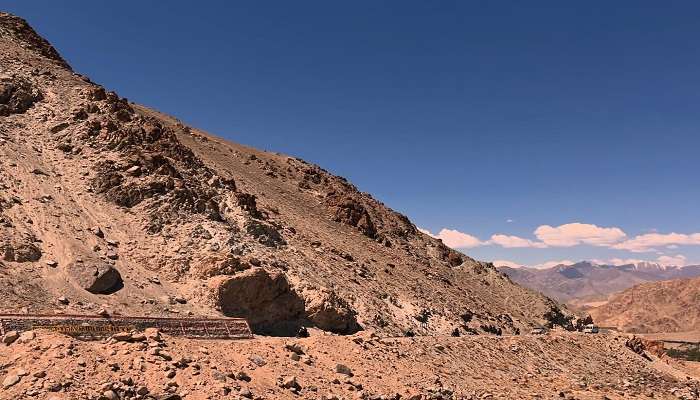 Panoramic view of Khardung-La Pass, with snow-capped mountains and a winding road going through rugged terrain in Ladakh, India.