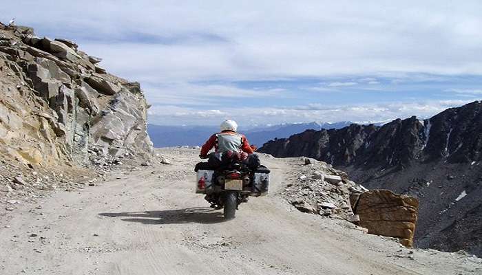 The Traveler Halts at Khardung-La Pass; in the backdrop is a panoramic view of mountainous landscapes with clear skies.