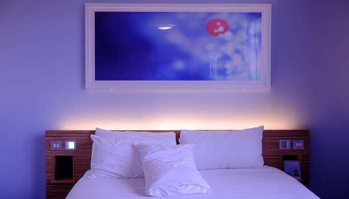 A hotel room with dim blue lights and a painting on the wall near Shri Bade Hanuman Ji Mandir