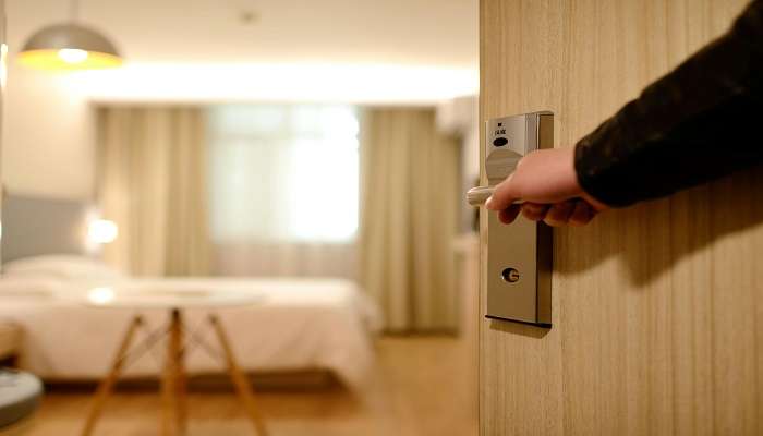 A person holding the door lever inside a hotel room