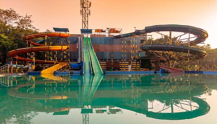 A scenic view of a swimming pool with turquoise clear water and a water slide at Neeladri Amusement and Water Parks .