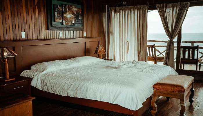 A double-size bed covered with white bedsheets and pillows with a perfect seaside view in hotels in Bapatla
