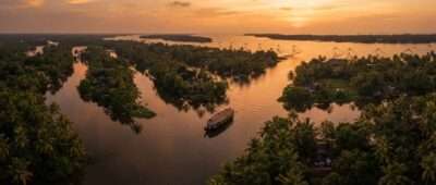 Aerial view of Ashtamudi Lake's palm-fringed arms with a Kettuvallam houseboat at sunset, Kollam, Kerala