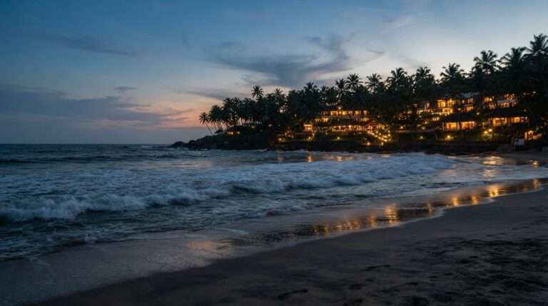 Waves rolling onto Kovalam beach at dusk with the resort lights behind the palms, Abad Harmonia, Kerala, India