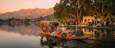 Destination wedding in Kashmir: flower-decked shikara crossing Dal Lake to a lakeside wedding lawn, Srinagar at sunset