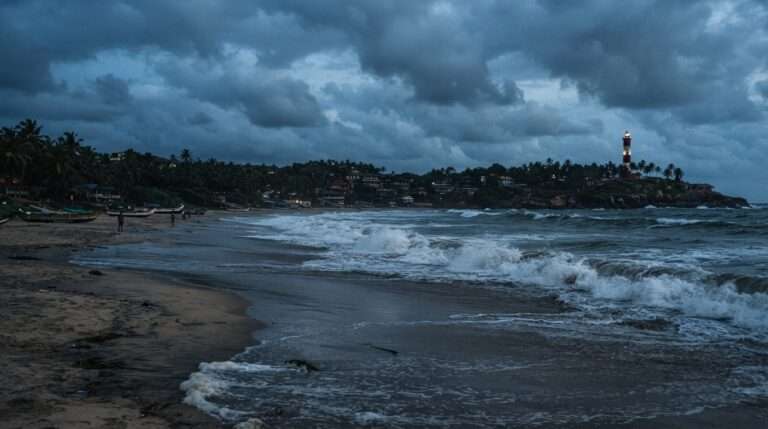 Rough monsoon surf rolling onto the crescent beaches under dramatic grey clouds, Kovalam, Kerala, India
