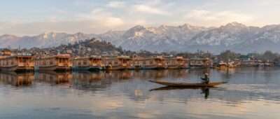 Shikara on Dal Lake at sunrise with houseboats and snow peaks, one of the best places to visit in Kashmir, India
